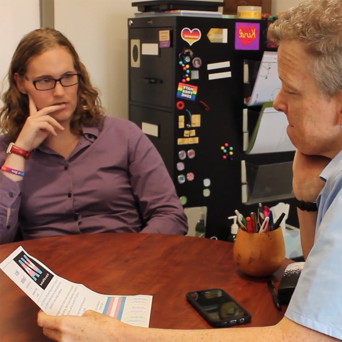 Photo of a student and professor Jen Morse speaking together in her office. There is a sticker in the background that says, HATE FREE ZONE