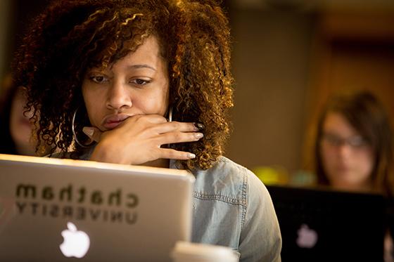 Photo of a woman working on her laptop with a Chatham University sticker in a lecture hall